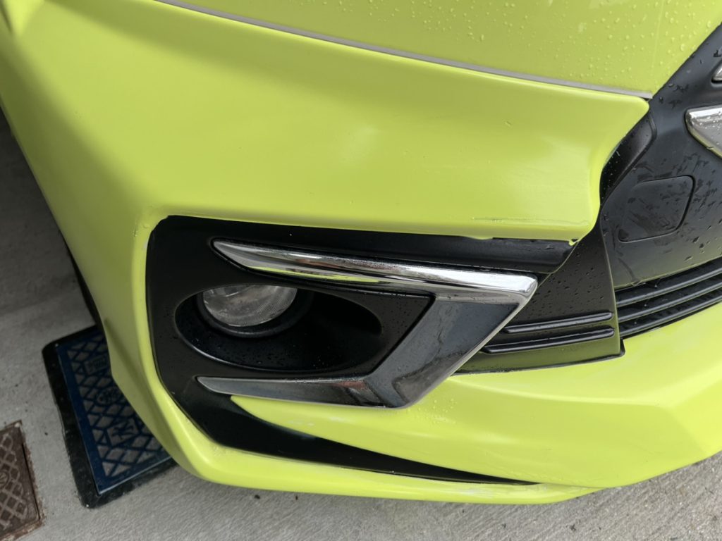 フロントバンパーに小さな線傷がある車。明るい黄緑のボディに浅い擦り傷が見られる。