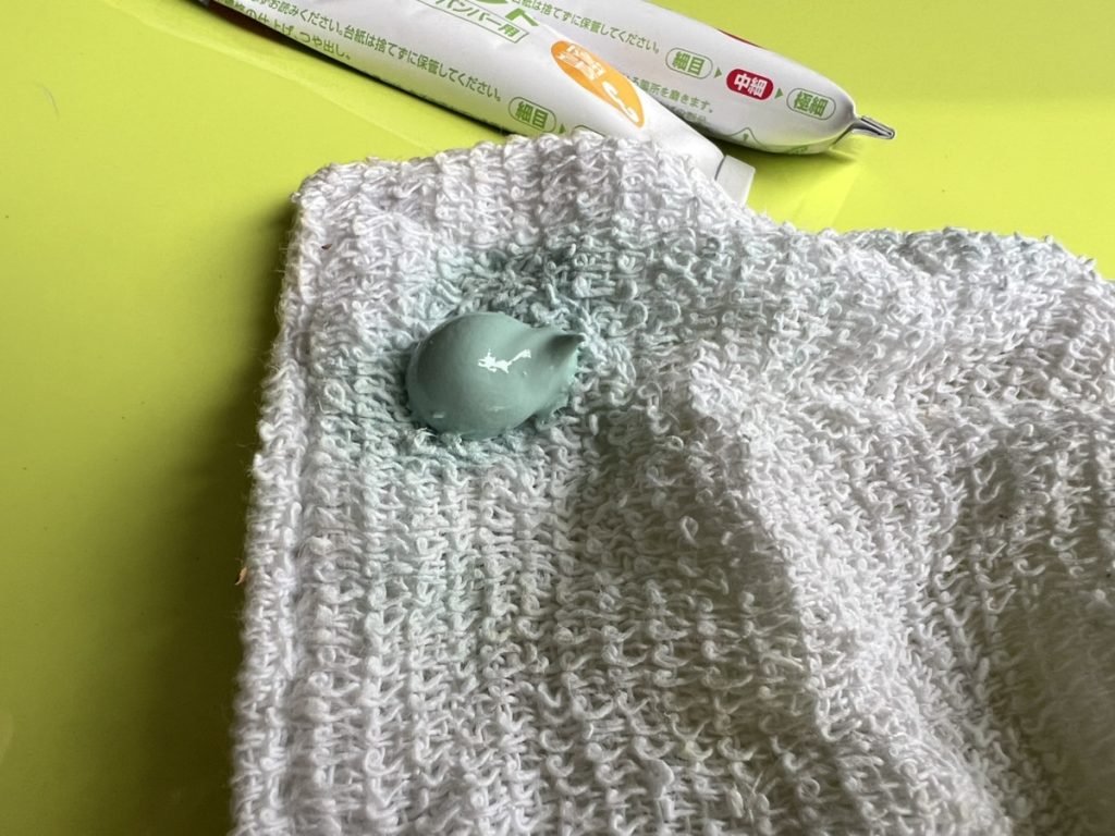 白いタオルの上に緑色のコンパウンドを出した状態。背景には黄緑色の車体と補修ペンが見える。